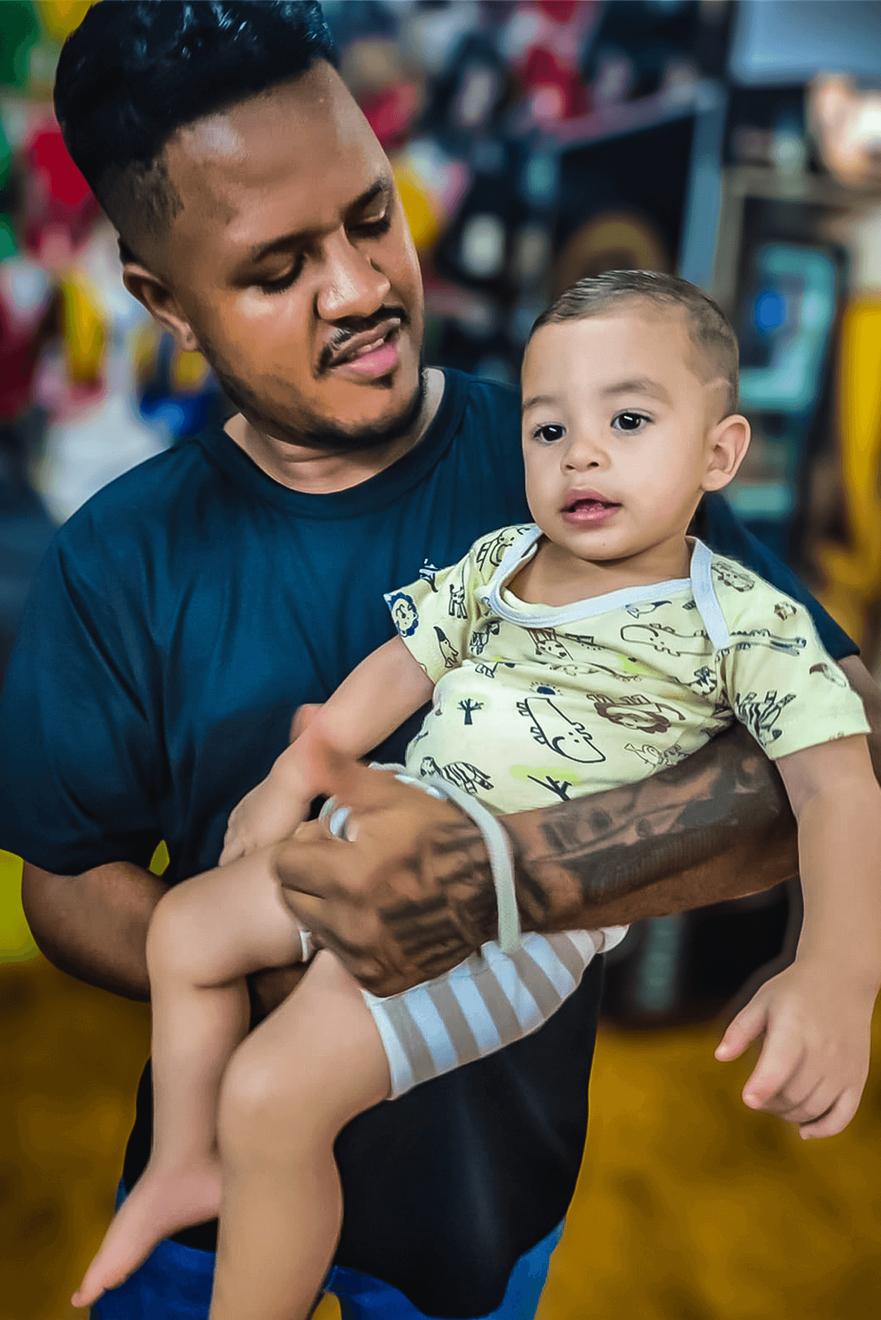 Marcelo, o experiente barbeiro e proprietário da Barbearia Santana em Rio Verde, segura carinhosamente uma criança no colo após finalizar o corte de cabelo da mesma, demonstrando sua gentileza e atenção com os clientes mirins.